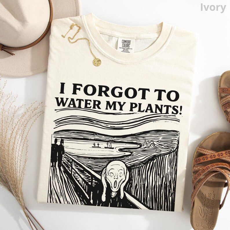 Peut inclure: T-shirt ivoire avec le texte "I FORGOT TO WATER MY PLANTS!" au-dessus d'un dessin en noir et blanc de "Le Cri" d'Edvard Munch. Un collier dor&eacute; et un chapeau beige sont visibles.