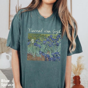 May include: A blue-green short-sleeve t-shirt featuring a printed graphic of Vincent van Gogh's Irises painting. The text Vincent van Gogh is printed in a light-coloured script font above the rectangular art reproduction on the chest.