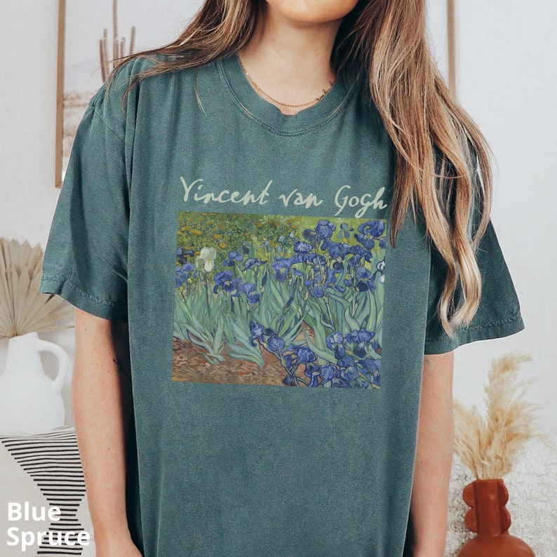 May include: A blue-green short-sleeve t-shirt featuring a printed graphic of Vincent van Gogh's Irises painting. The text Vincent van Gogh is printed in a light-coloured script font above the rectangular art reproduction on the chest.