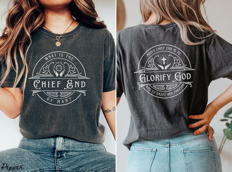 May include: A dark gray t-shirt with a white graphic design on the front and back. The front design says "What is the Chief End of Man?" with a cross and hands in a circle. The back design says "Man's Chief End is to Glorify God and to Enjoy Him Forever" with a cross and hands in a circle.