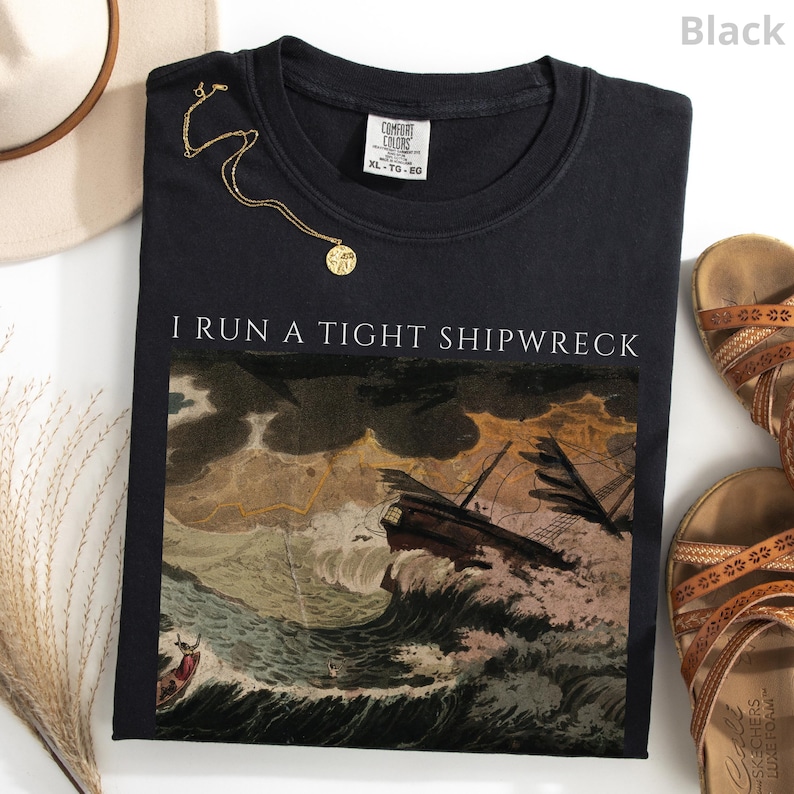 May include: Black crew neck sweatshirt with the text "I RUN A TIGHT SHIPWRECK" above a graphic of a ship in a storm. A gold necklace and brown sandals are also visible.