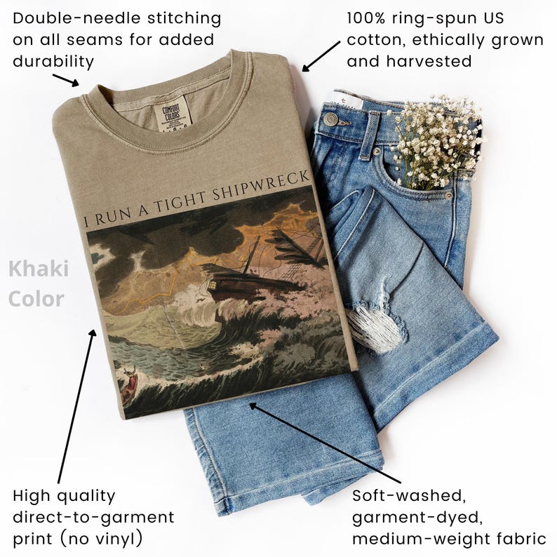 May include: Khaki-colored t-shirt with the text "I RUN A TIGHT SHIPWRECK" and a graphic of a ship in a storm. The shirt is made of soft, medium-weight, garment-dyed cotton. The image also shows a pair of blue jeans.