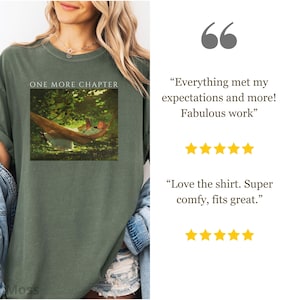 May include: Olive green t-shirt with the text "ONE MORE CHAPTER" above a framed image of a person in a hammock. The shirt is worn by a person with blonde hair and a denim jacket.