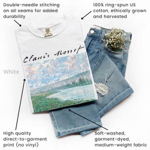 May include: White t-shirt with a painting of a river and mountains. The text "Claude Monet" is written in black ink on the shirt. The shirt is made of 100% ring-spun US cotton and is double-needle stitched for durability.