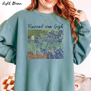 May include: Light green sweatshirt with a print of a painting by Vincent van Gogh featuring a field of blue irises.