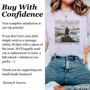 May include: A light purple t-shirt with the text "HANG ON, LET ME OVERTHINK THIS" printed on the front. The text is in a black font and is centered on the shirt. The shirt is being worn by a person, and the bottom of the shirt is tucked into a pair of blue jeans.
