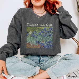 May include: A dark gray sweatshirt with a cropped fit features a vintage-style print of Vincent van Gogh's Irises painting. The print is in the center of the sweatshirt and includes the artist's name.