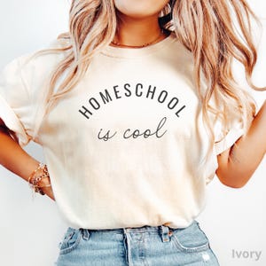 May include: A white t-shirt with the text "HOMESCHOOL is cool" in black lettering. The shirt is being worn by a person with long blonde hair.