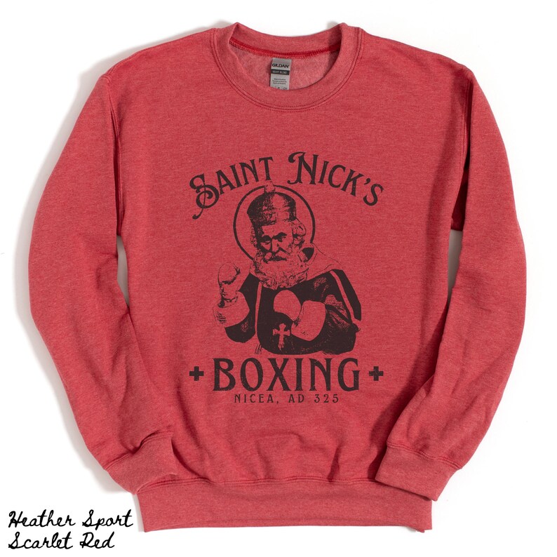 Op de afbeelding: Rood heather sweatshirt met een zwart-witte illustratie van Sinterklaas die boksen. De tekst "SAINT NICK'S + BOXING + NICEA, AD 325" staat op het sweatshirt gedrukt.