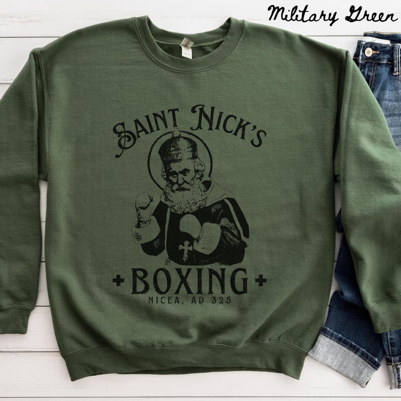 Op de afbeelding: Een groen sweatshirt met een zwarte afbeelding van Sinterklaas die boksen. De afbeelding bevat de tekst "Saint Nick's Boxing" en "Nicaea, AD 325".