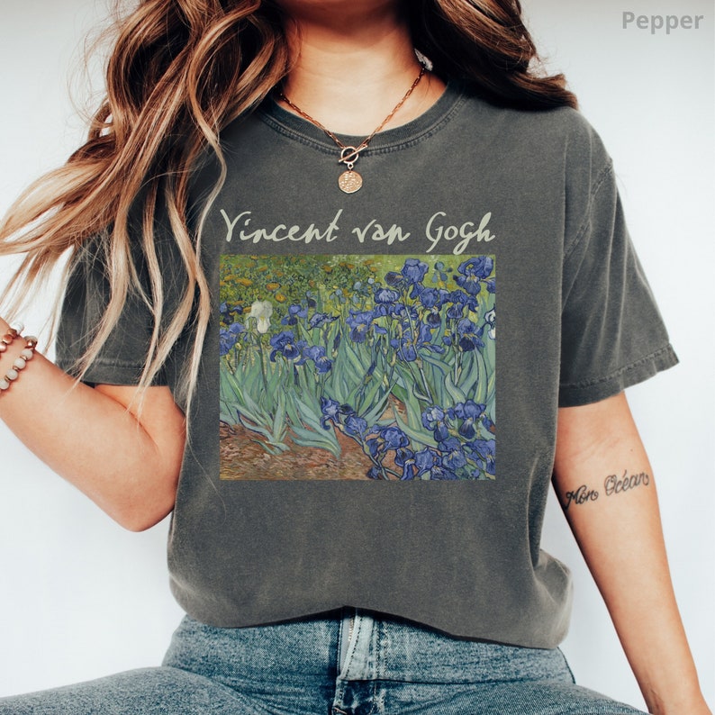 May include: A charcoal grey short-sleeve t-shirt featuring a printed reproduction of Vincent van Gogh's Irises painting. The text Vincent van Gogh is printed in a light beige font above the artwork. The shirt has a crew neckline and a relaxed fit.