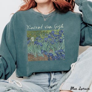 May include: A teal blue sweatshirt with a vintage-style print of Vincent van Gogh's Irises painting. The text "Vincent van Gogh" is printed in white above the painting.