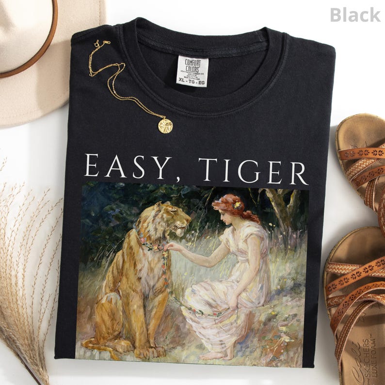 May include: Black crew neck sweatshirt with the text "EASY, TIGER" above a painting of a woman and a tiger. A gold necklace and brown sandals are next to the shirt. The shirt is a Comfort Colors XL-TG-EG.