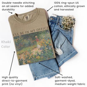 May include: Khaki-colored t-shirt with the text "I'LL BE IN MY OFFICE" and a floral painting. The shirt is paired with blue jeans. Features include double-needle stitching, high-quality direct-to-garment print, and 100% ring-spun US cotton.