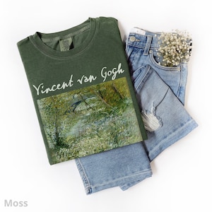 May include: A green t-shirt with a painting by Vincent van Gogh printed on the front. The painting depicts a bridge over a stream with trees and foliage in the background.