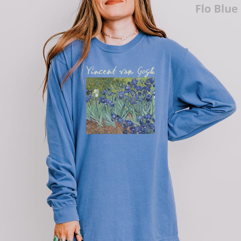 May include: A long-sleeve crewneck sweatshirt in a solid Flo Blue colour. The front features a rectangular graphic print of Vincent van Gogh's Irises painting, with the text "Vincent van Gogh" printed in a light yellow script font above the artwork.