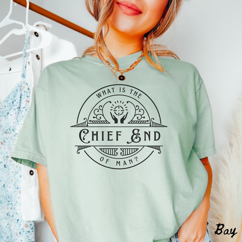 May include: A light green t-shirt with a black graphic design that reads "What is the Chief End of Man?" The graphic is a circle with a cross in the center and two hands reaching up to the cross.