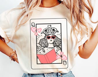 Peut inclure: Sweat-shirt ivoire avec un motif de carte à jouer. La carte représente la Reine de Cœur portant des lunettes de soleil en forme de cœur et une couronne, tenant un livre rose. Des cœurs roses entourent la carte. Le mot "Ivory" est imprimé en bas à droite.