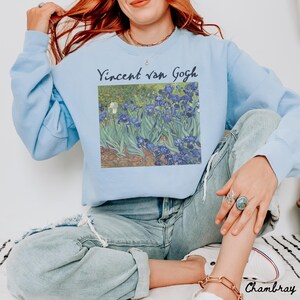May include: A light blue sweatshirt with a graphic print of Vincent van Gogh's Irises painting. The text "Vincent van Gogh" is printed above the painting.