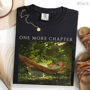 May include: Black Comfort Colors sweatshirt with the text "ONE MORE CHAPTER" above an image of a person reading in a hammock. A gold necklace and brown sandals are also visible.