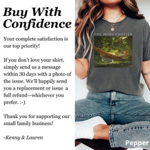 May include: A dark gray t-shirt with the text "ONE MORE CHAPTER" above a framed image of a person in a hammock. The shirt also has the text "Buy With Confidence" and other text on the left side.