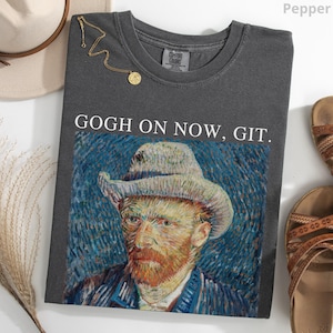 May include: A dark gray t-shirt with the text "GOGH ON NOW, GIT." above a print of Vincent van Gogh's self-portrait. The shirt is styled with a gold necklace and sandals.