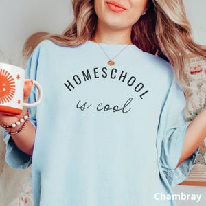May include: A light blue t-shirt with the text "HOMESCHOOL is cool" printed in black. The shirt is made of a soft, comfortable fabric and has a relaxed fit.