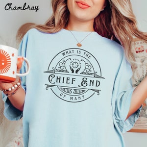 May include: Light blue t-shirt with a black graphic design of a circle with the text "What is the Chief End of Man?" inside. The graphic design features a stylized image of two hands holding a sun with a cross in the center.