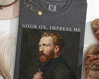 May include: Dark gray t-shirt with the text "GOGH ON, IMPRESS ME" above a portrait of Vincent van Gogh. The shirt is a Comfort Colors brand. A gold necklace and sandals are also visible.