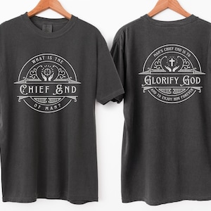 May include: A dark gray t-shirt with a white graphic on the front that reads "What is the Chief End of Man?" and a white graphic on the back that reads "Man's Chief End is to Glorify God and to Enjoy Him Forever."