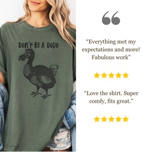 May include: Olive green t-shirt featuring a black illustration of a dodo bird and the text "DON'T BE A DODO". The shirt has a relaxed fit and short sleeves. The shirt is made of a soft, comfortable material.