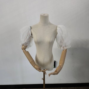 May include: White sheer fabric puff sleeves on a dress form. The sleeves are gathered at the top and have a ruffled edge.