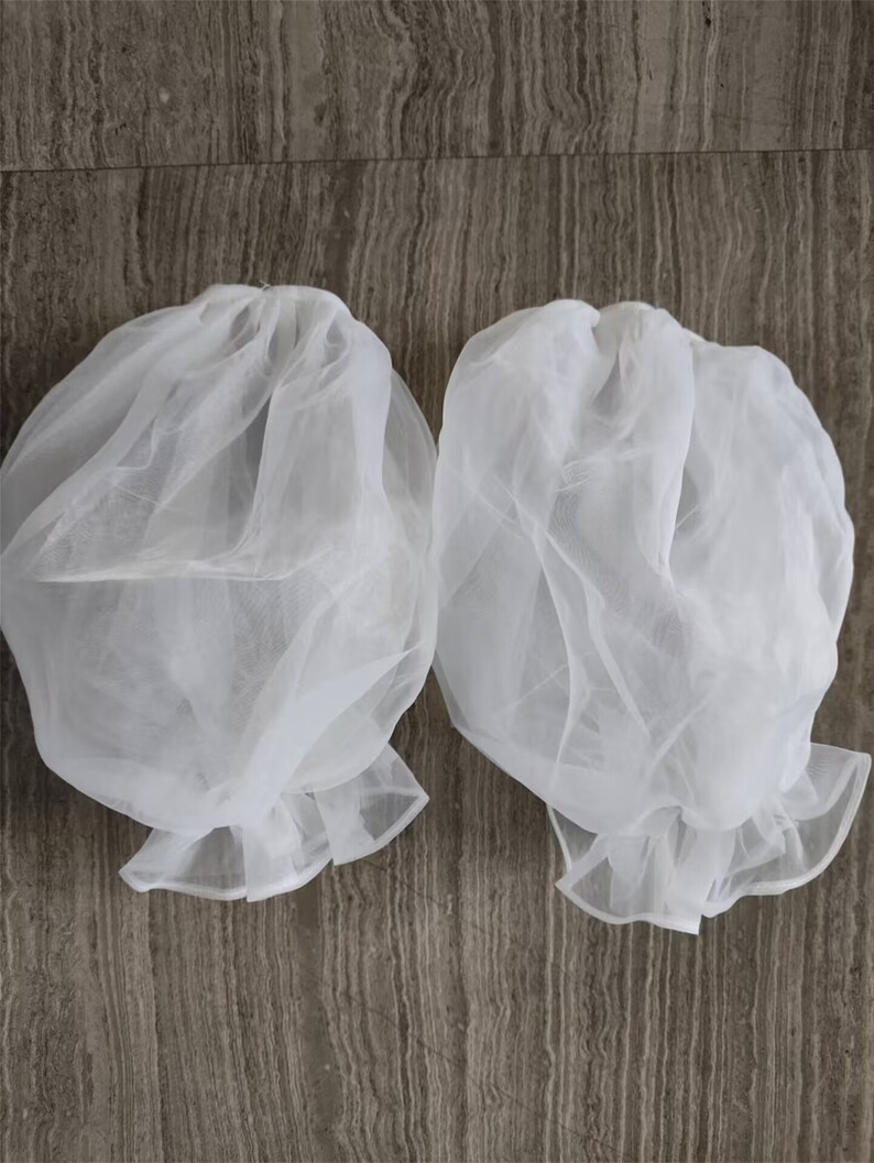 May include: Two white tulle fabric puff sleeves with ruffled edges.