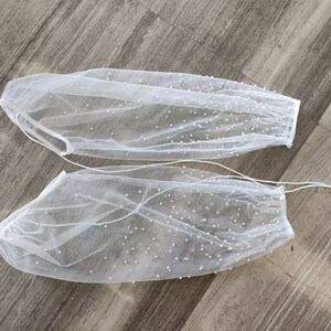Peut inclure: Une paire de manches en tulle blanc avec des embellissements de perles. Les manches sont transparentes et ont un &eacute;lastique pliss&eacute; en haut.