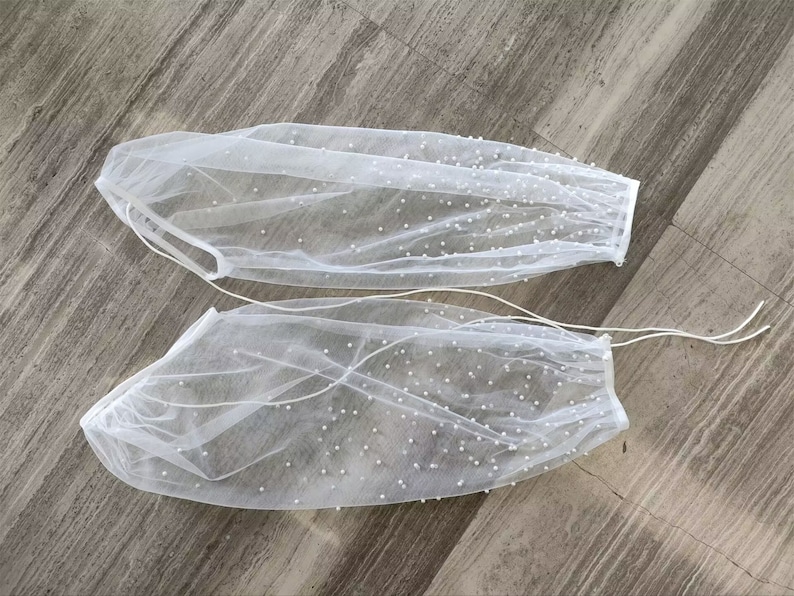 Peut inclure: Une paire de manches en tulle blanc avec des embellissements de perles. Les manches sont transparentes et ont un &eacute;lastique pliss&eacute; en haut.