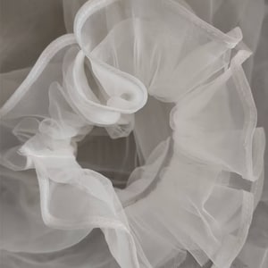 May include: White tulle fabric with a ruffled edge. The fabric is soft and delicate, and it has a slightly sheer appearance.