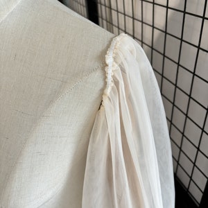 May include: Close-up of a white sheer fabric sleeve with a gathered elastic band at the top.