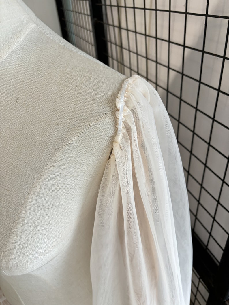 May include: Close-up of a white sheer fabric sleeve with a gathered elastic band at the top.