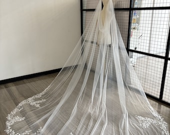 May include: A white bridal veil with a delicate floral lace trim. The veil is made of soft tulle and is long and flowing.