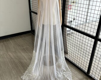 May include: A long, white bridal veil with a delicate lace trim and a blush pink lining. The veil is displayed on a mannequin.