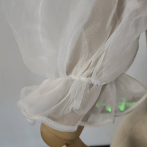 May include: Close-up of a white sheer fabric with a ruffled edge. The fabric is delicate and translucent, with a soft, flowing texture.