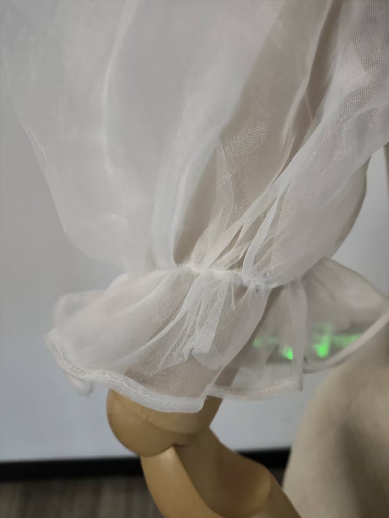 May include: Close-up of a white sheer fabric with a ruffled edge. The fabric is delicate and translucent, with a soft, flowing texture.