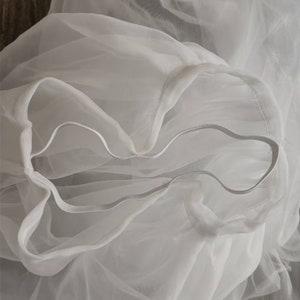 May include: White tulle fabric with a gathered edge. The fabric is soft and sheer, and it is perfect for making a variety of garments and accessories.
