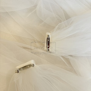 May include: Two white tulle veils with silver clips attached. The veils are layered and have a soft, delicate texture.