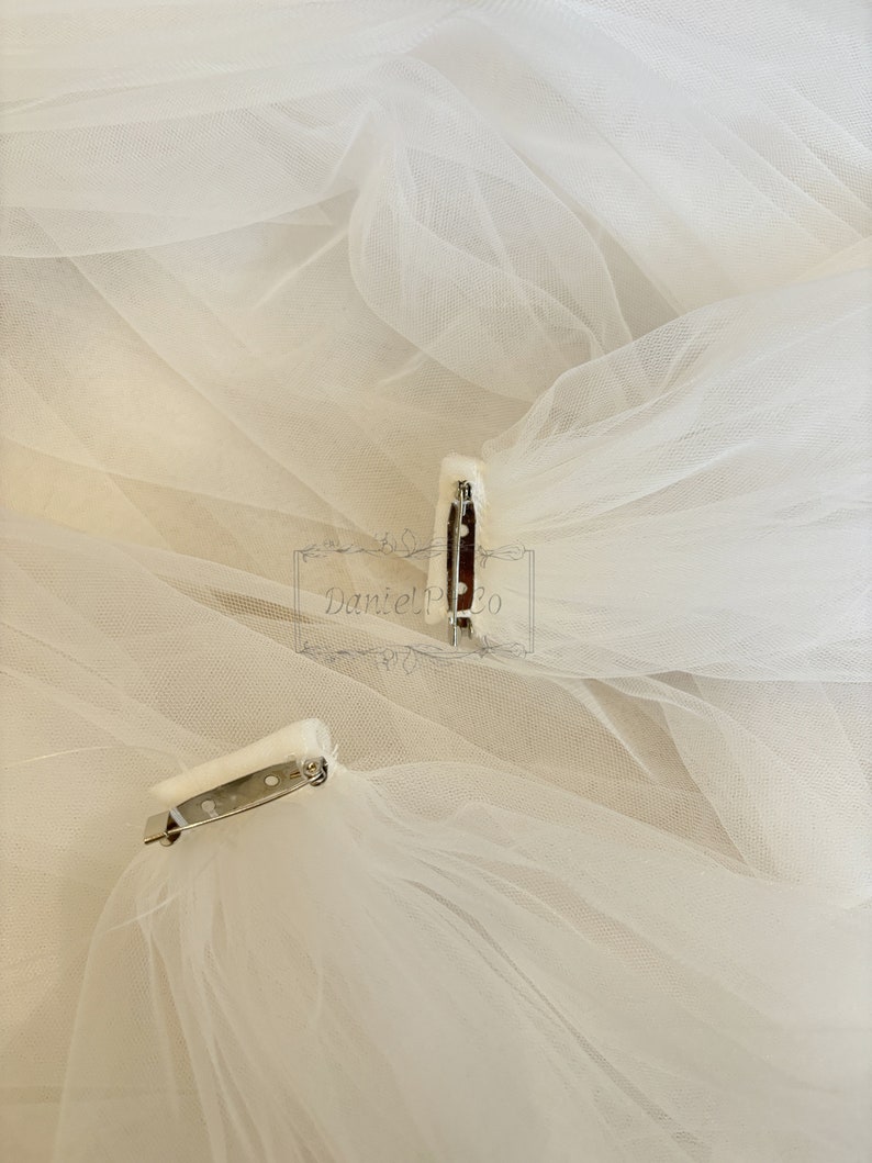 May include: Two white tulle veils with silver clips attached. The veils are layered and have a soft, delicate texture.