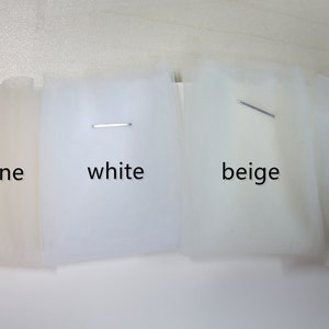 Puede incluir: Cuatro muestras de tejido de tul en diferentes tonos de blanco: champ&aacute;n, blanco, beige y marfil.