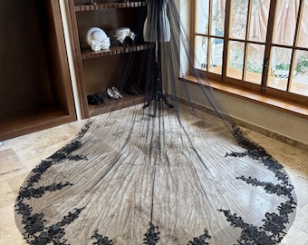 May include: A black tulle wedding veil with a black lace trim. The veil is long and flowing, and the lace trim is delicate and intricate.