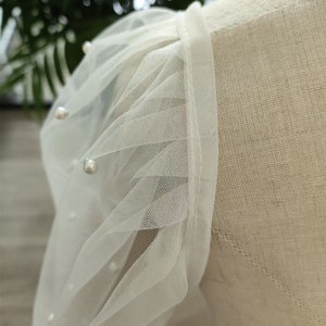 Peut inclure: Tissu de tulle blanc avec des embellissements de perles. Le tulle est fronc&eacute; et pliss&eacute;, cr&eacute;ant un look d&eacute;licat et f&eacute;minin.