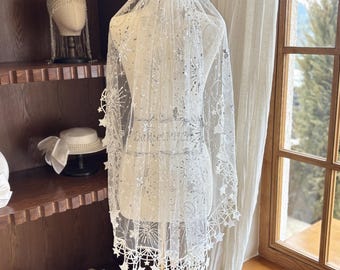 May include: White tulle veil with silver glitter stars and a scalloped edge. The veil is displayed on a mannequin in a room with a window.