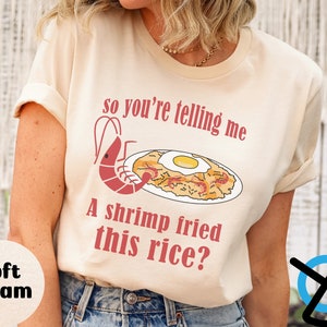 May include: A cream colored t-shirt with a shrimp fried rice illustration and the text "So you're telling me a shrimp fried this rice?"